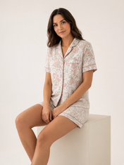 Mujer sentada con pijama Susurro Floral Amore Eco White de algodón Pima, en estudio. Imagen generada con IA sobre la prenda real.